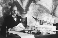 a man in a suit sitting at a desk with papers